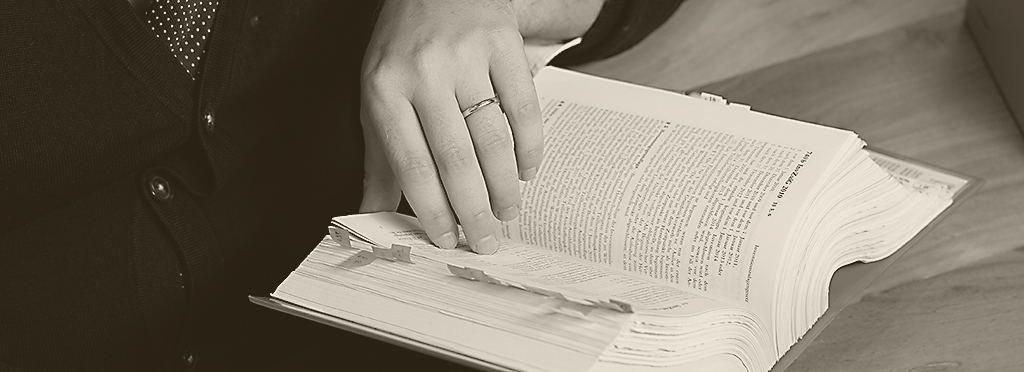Hand mit Ehering blättert in aufgeschlagenem Buch, Anzugärmel, Detailaufnahme, Schwarz-Weiß-Foto betont Textur und Kontrast.